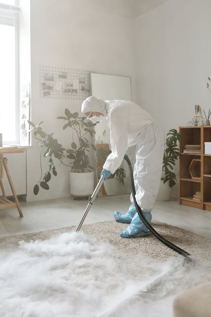 A red handheld vacuum cleaner resting on a beige carpet in a residential room with hardwood flooring, partially visible wooden furniture, and a person barefooted standing on the carpet. The vacuum appears to be in use or ready for surface cleaning, with a focus on maintaining hygiene and tidiness in the home. The room is well-lit, highlighting the clean and orderly surface, aligning with the services offered by Islington Carpet Cleaners on their page about same day carpet cleaning delays and common problems in Islington.